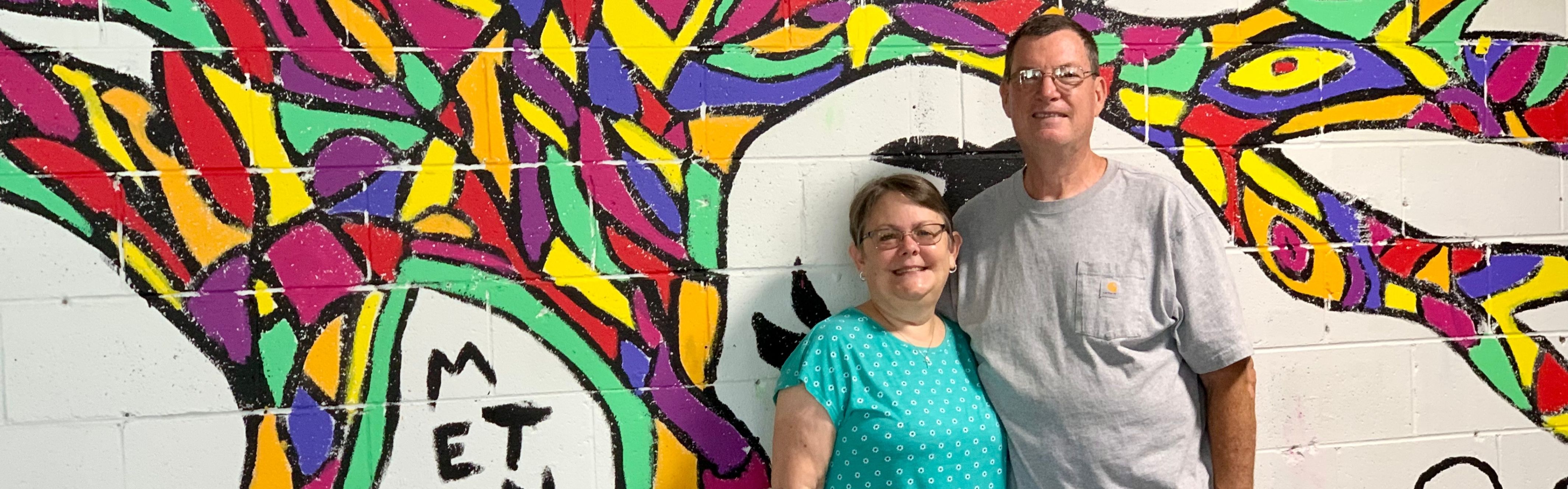 couple standing in front of wall painted with colorful mural