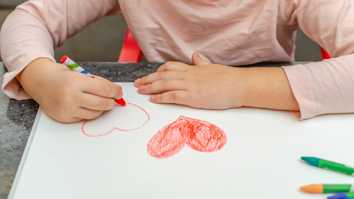 Hands of young child drawing hearts on paper.