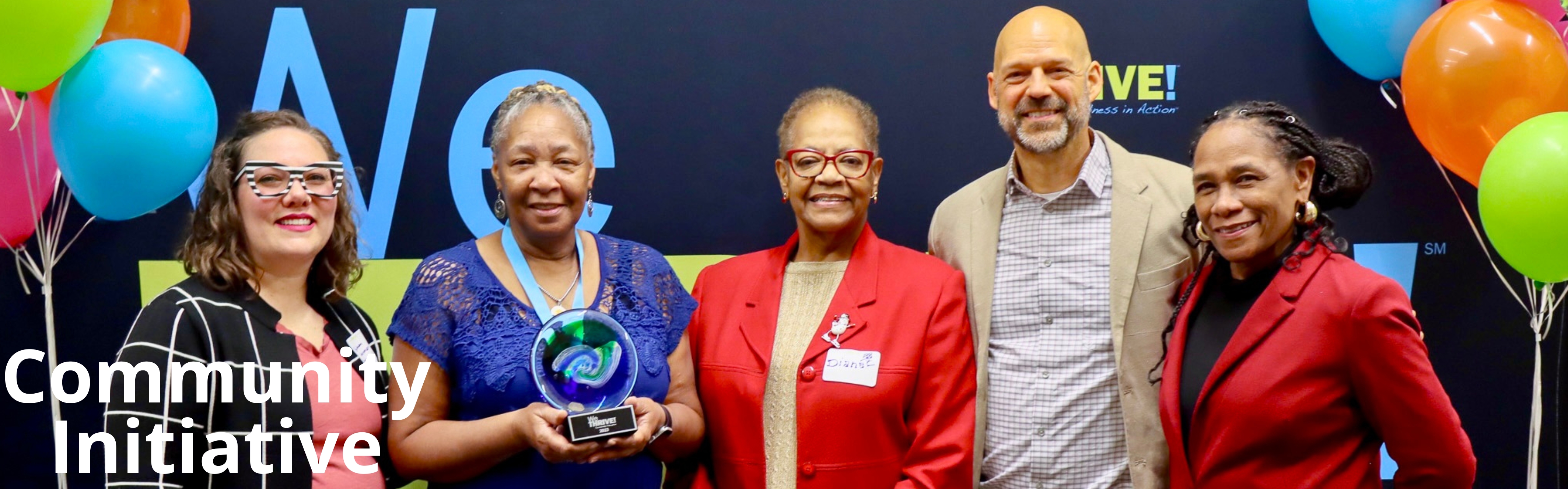 Five adults standing in front of we thrive banner with balloons on each side.