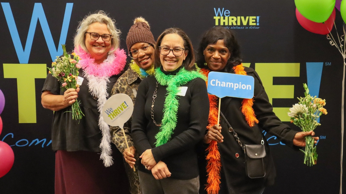 Group of four women from North College Hill, Ohio WeTHRIVE! team posting in front of banner.