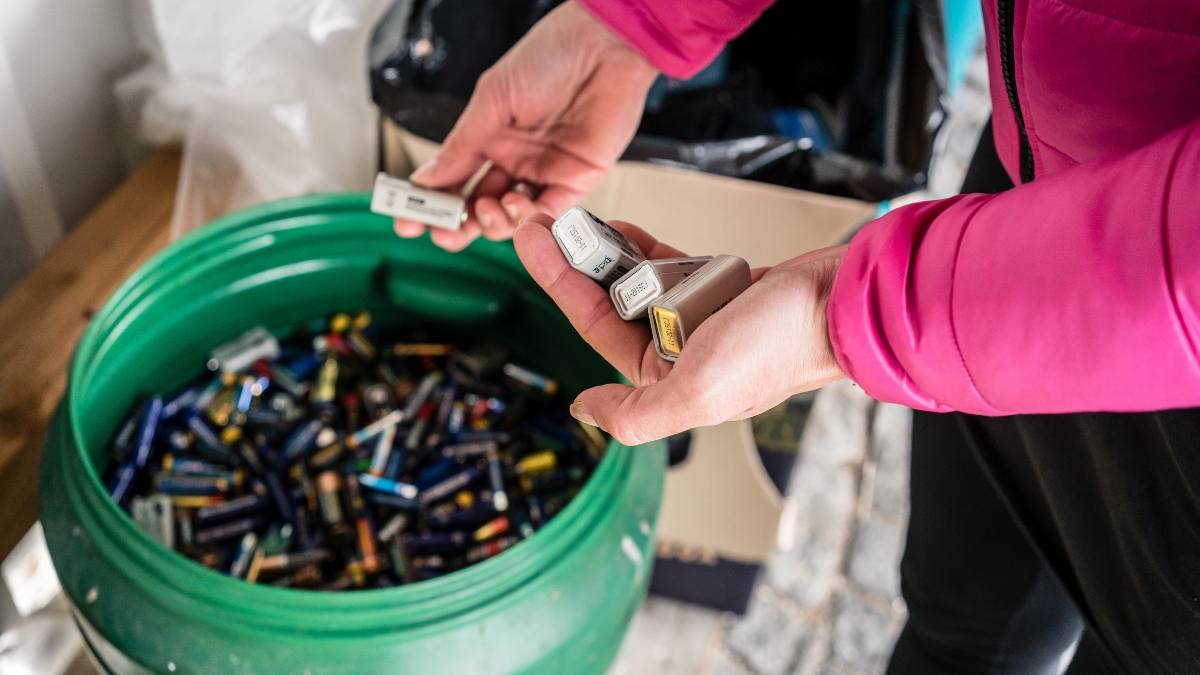 Bucket of old batteries with the hands of a person adding more.
