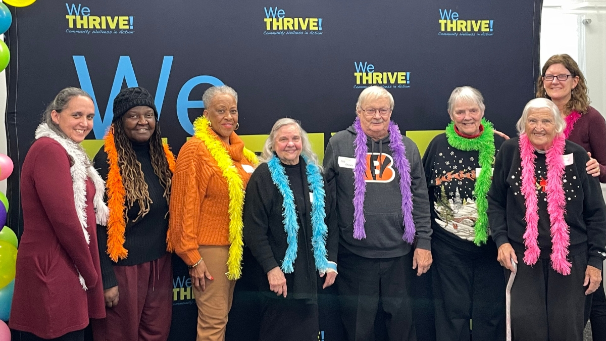 Eight adults posing in front of a WeTHRIVE! banner.