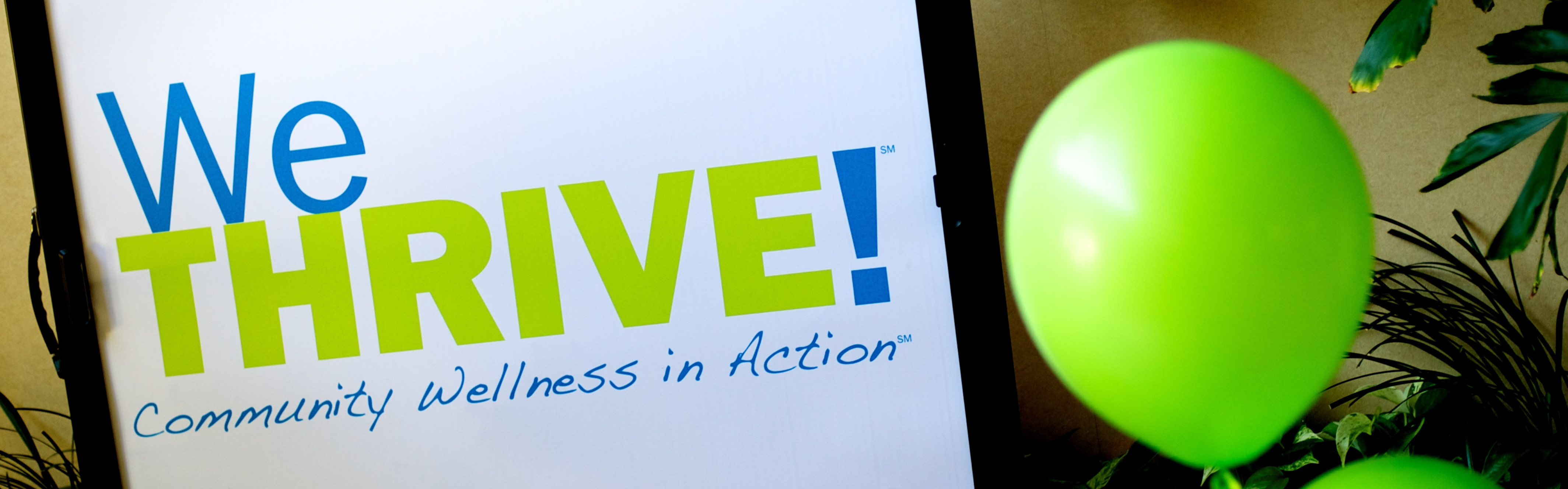WeThrive logo on signboard next to green balloon.